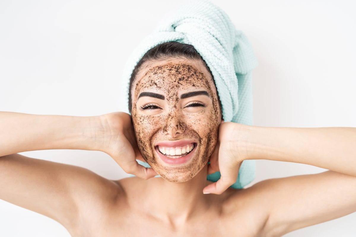 young smiling woman applying coffee scrub mask on face happy girl having skin care spa day at home healthy alternative natural exfoliation treatment and people lifestyle concept