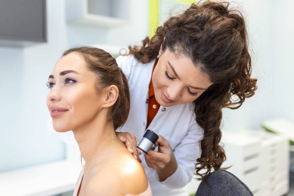 female dermatologist carefully examining the skin of a female patient using a dermascope, looking for signs of skin cancer. dermatologist examining patient's birthmark with magnifying glass in clinic