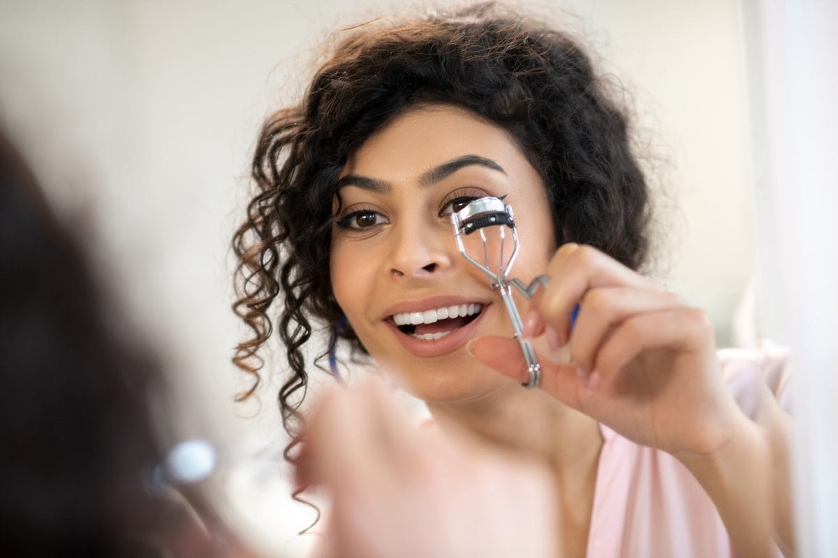 beautiful dark haired woman curling her eyelashes with a curler