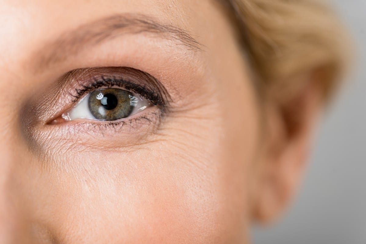 selective focus of mature woman looking at camera isolated on grey