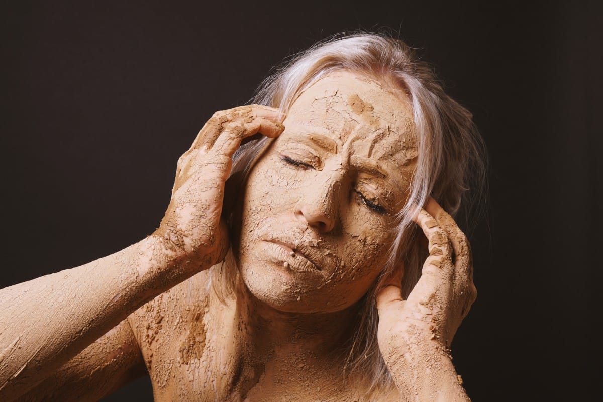 woman covered in dry cracked clay mud mask holding her head