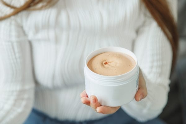 woman holds cosmetic jar with wax or clay product