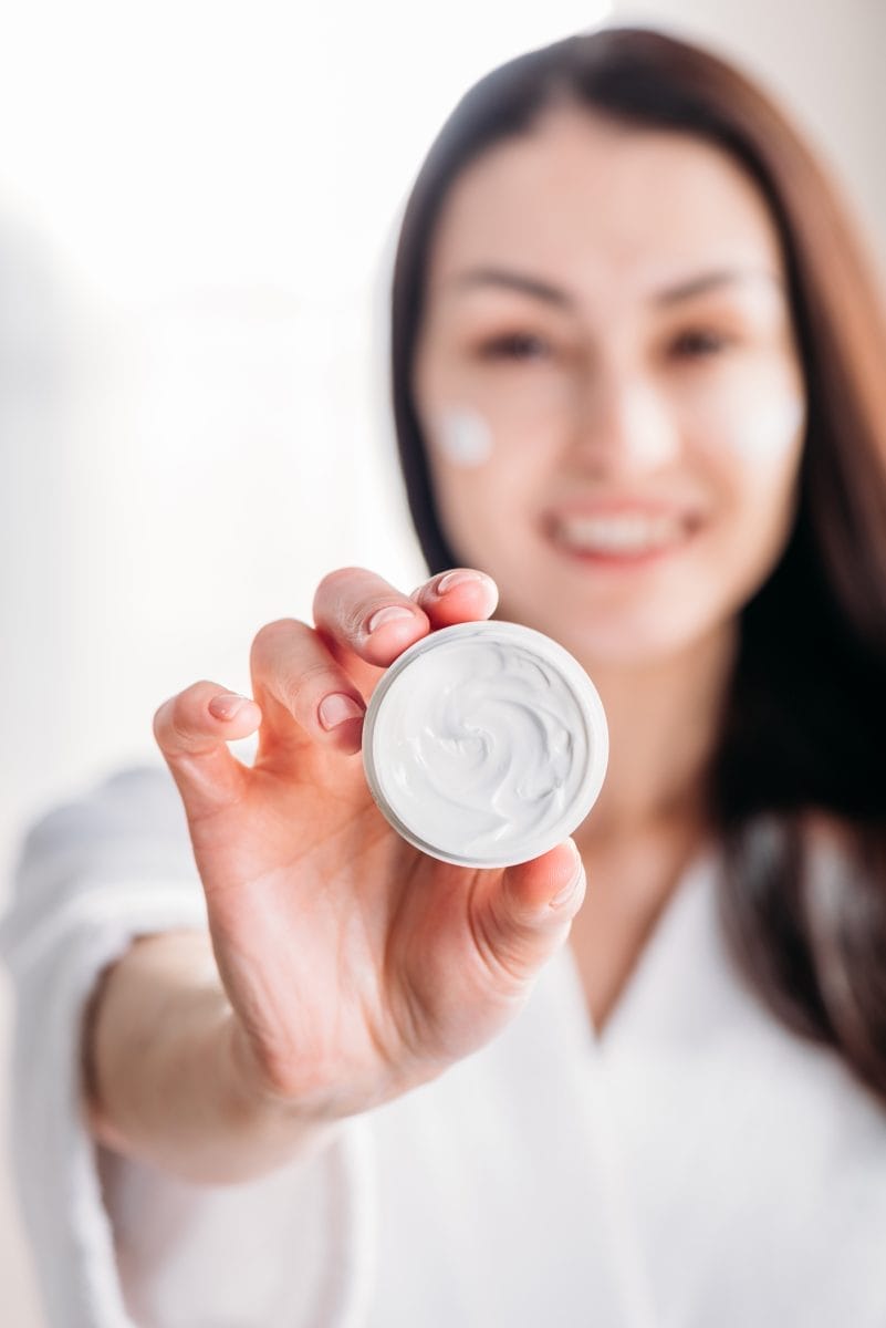 young smiling woman showing an open jar of face cream