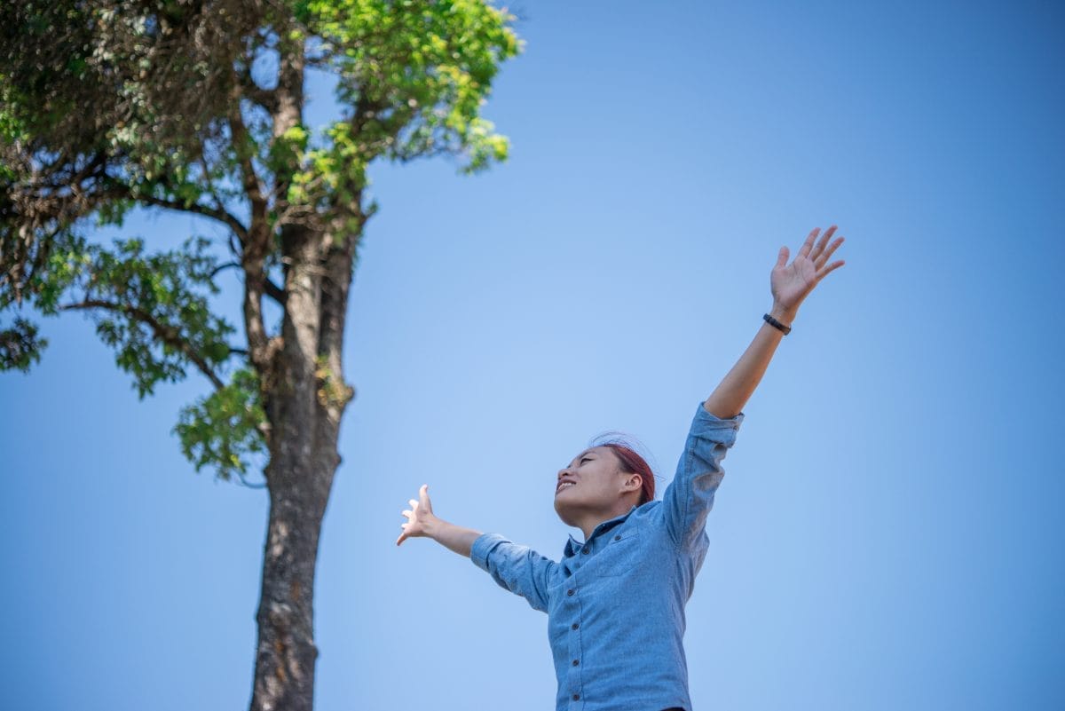 young woman standing looking to a sky with raised hands while du