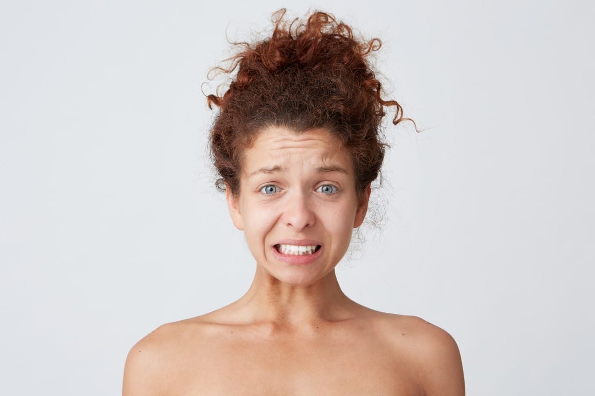 close up shot of upset worried young woman with curly hair and heathy skin after applying mask or cream feels confused and embarrassed isolated over white backgrond