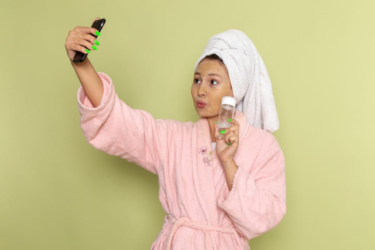 a front view young attractive female in pink bathrobe taking a selfie with spray on the green background lady bath model beauty