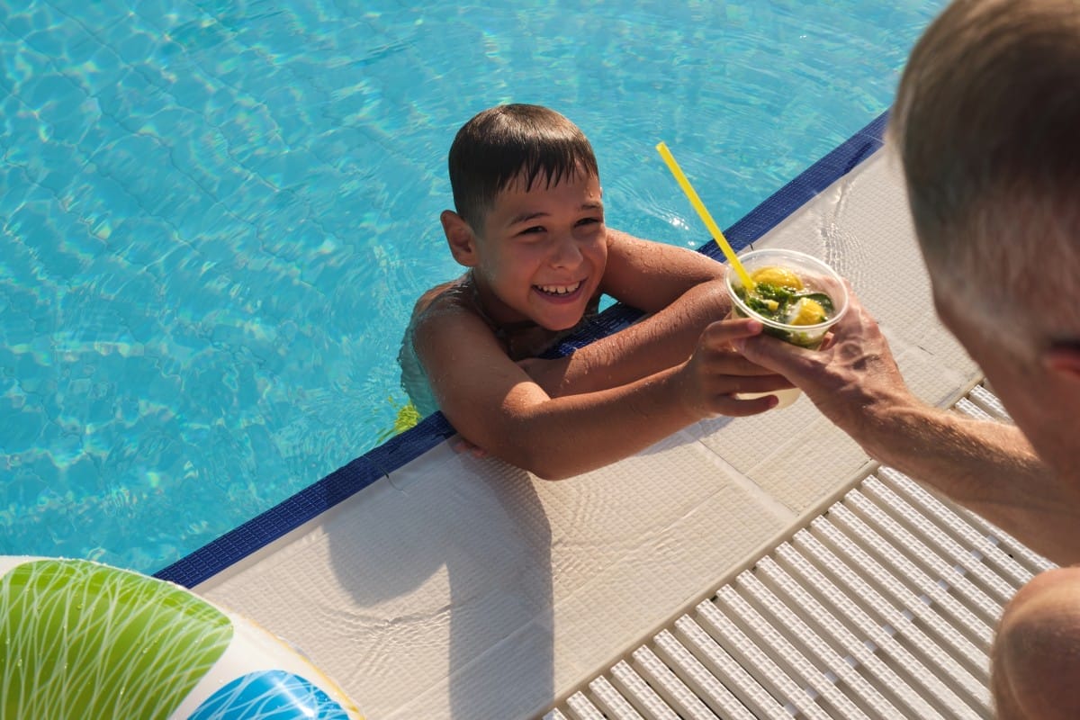 a gleeful child resting at the pool's edge, being handed a cool citrus beverage, symbolizing carefree summer days and moments of refreshment