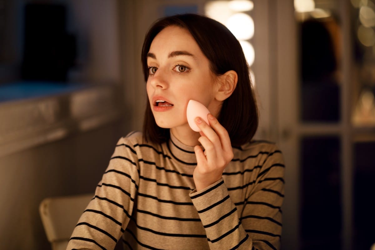 beautiful young woman applying makeup foundation, using sponge