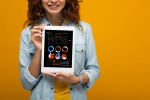 cropped view of happy curly girl holding digital tablet with charts and graphs on screen isolated on