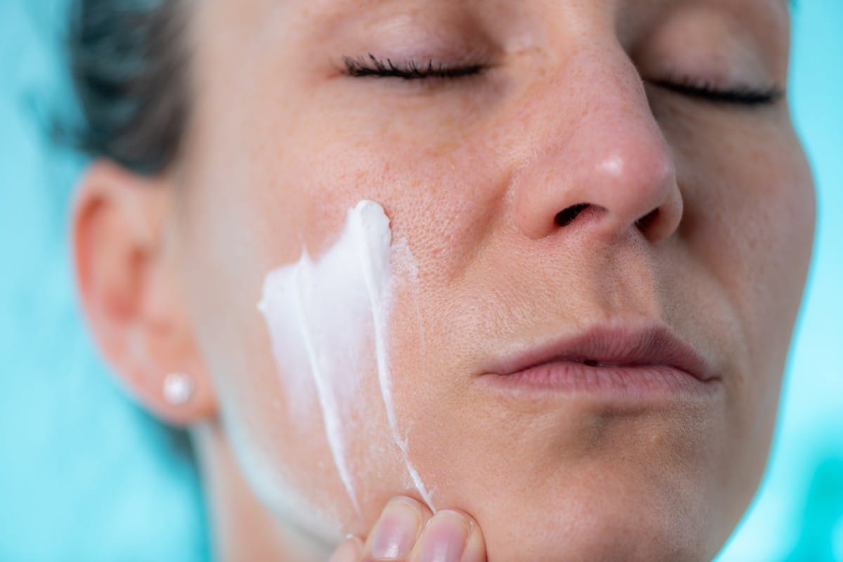 woman applies cream to her face at home