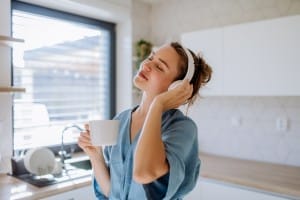 young woman listening music and enjoying cup of coffee at morning, in her kitchen.