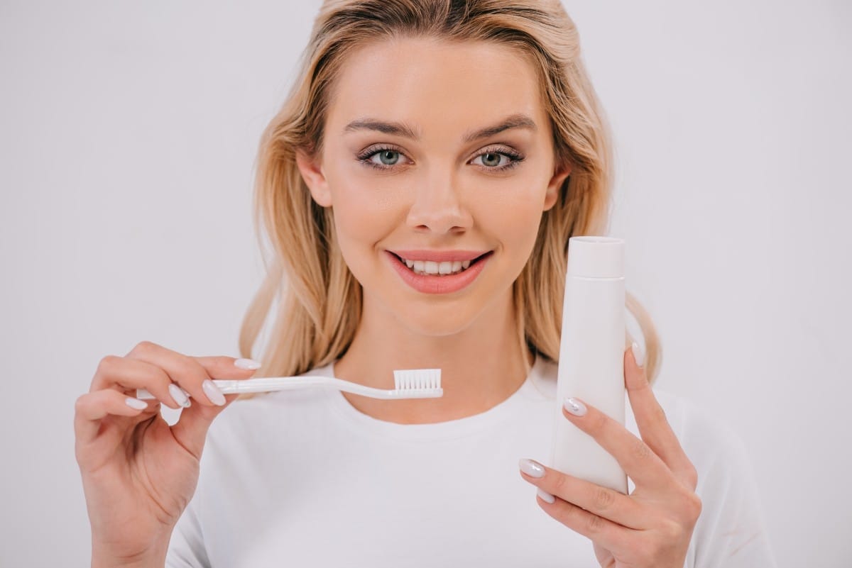 beautiful woman looking at camera while holding toothbrush and toothpaste with copy space isolated