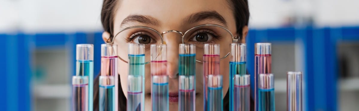 preteen girl in eyeglasses looking at camera near test tubes in lab, banner