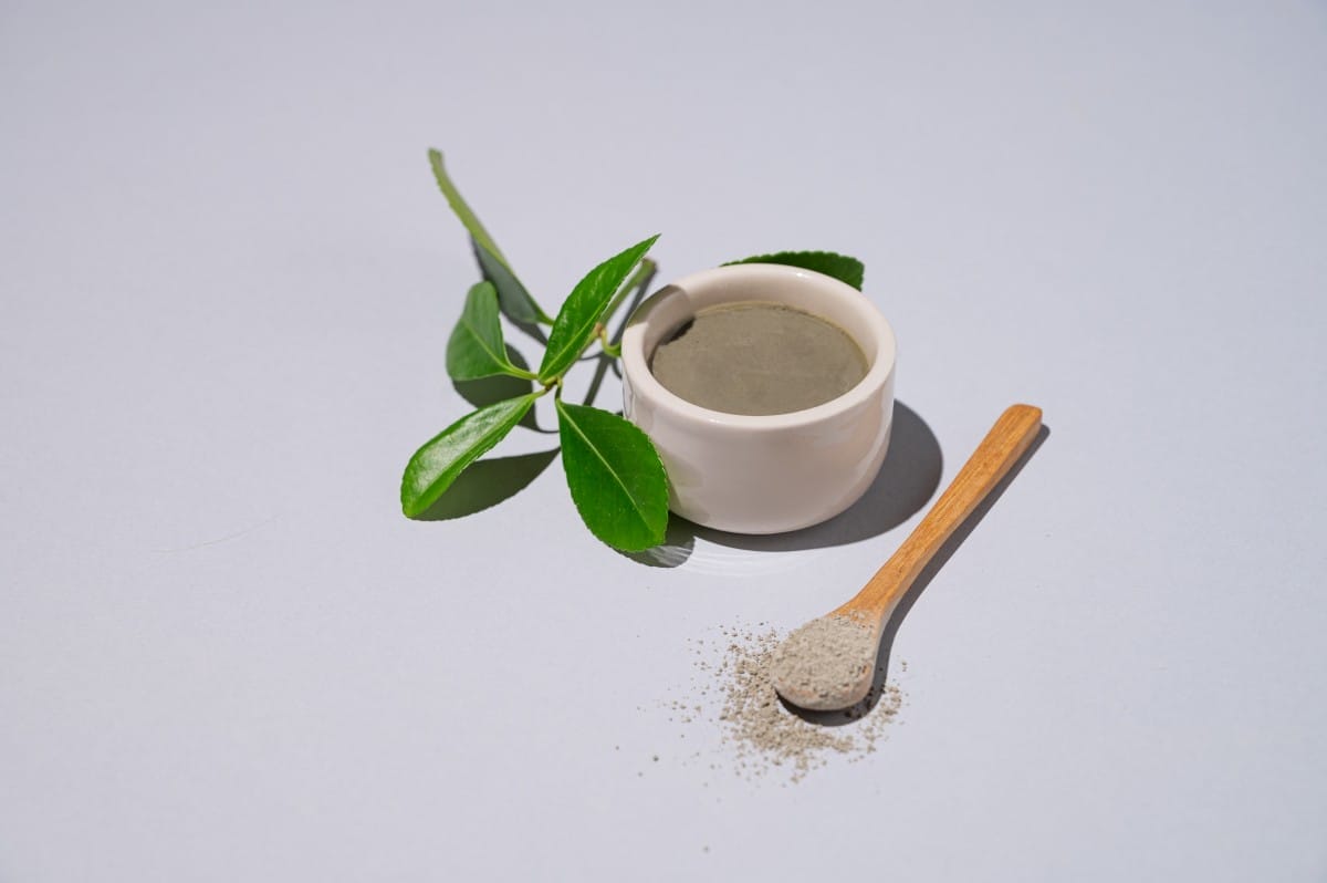 spa treatment. blue clay in a bowl and spoon on a light background with leaves and shadow.