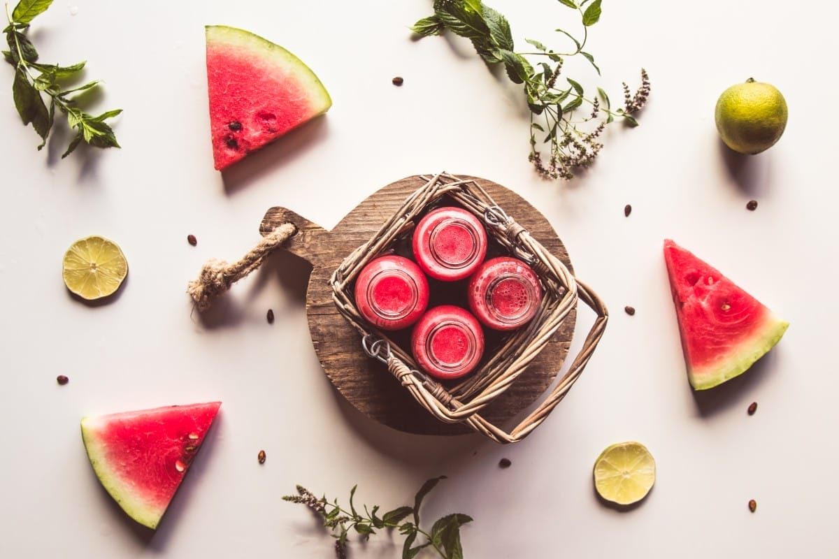 tasty summer bottled watermelon drink in a basket and slices of fresh fruits on white background