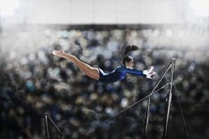 a female gymnast, a young woman performing on the parallel bars, in mid flight reaching towards the top bar.