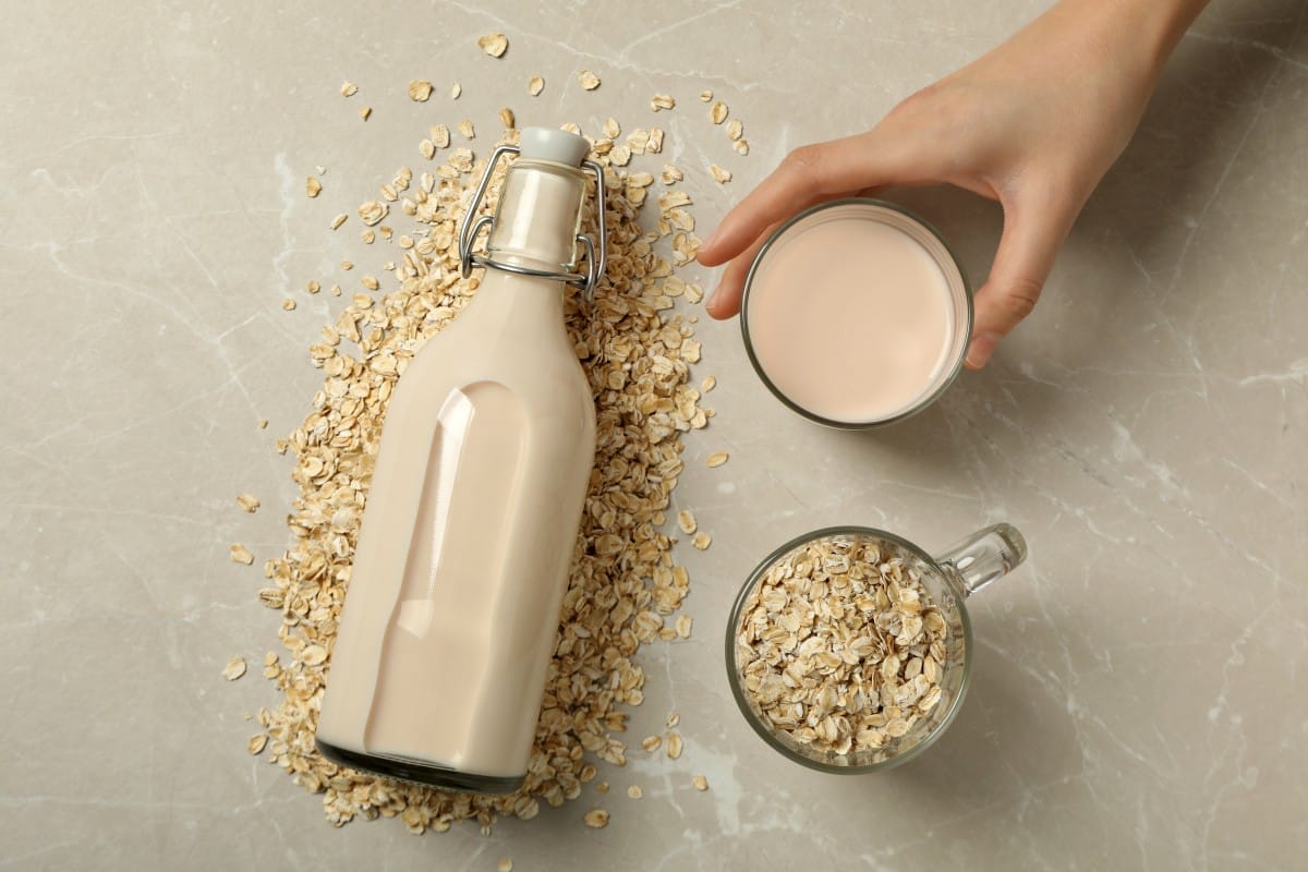 bottle and glass with milk, oatmeal and hand on beige background