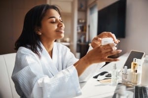 cheerful young woman holding jar of cosmetic cream