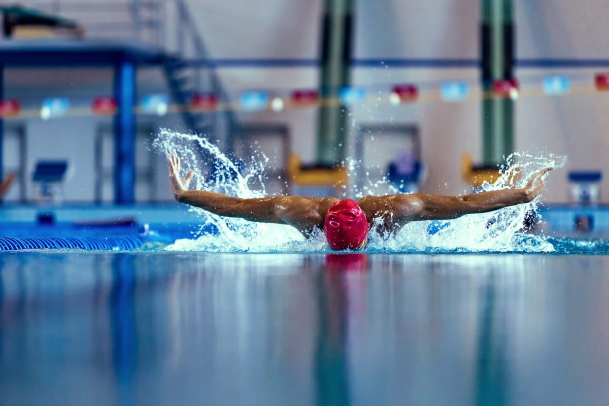 professional male swimmer in swimming cap and goggles in motion and action during training at pool, indoors. healthy lifestyle, power, energy, sports movement concept