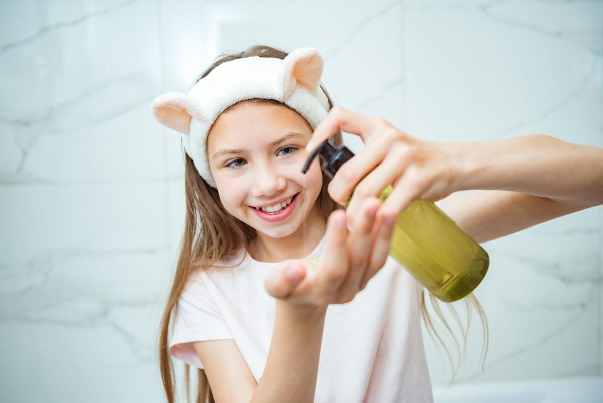 Young girl applying skincare in bathroom, smiling.