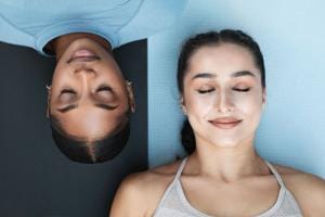 Two women relaxing on yoga mats, eyes closed