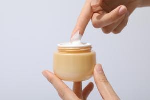 Hand applying cream from jar on white background