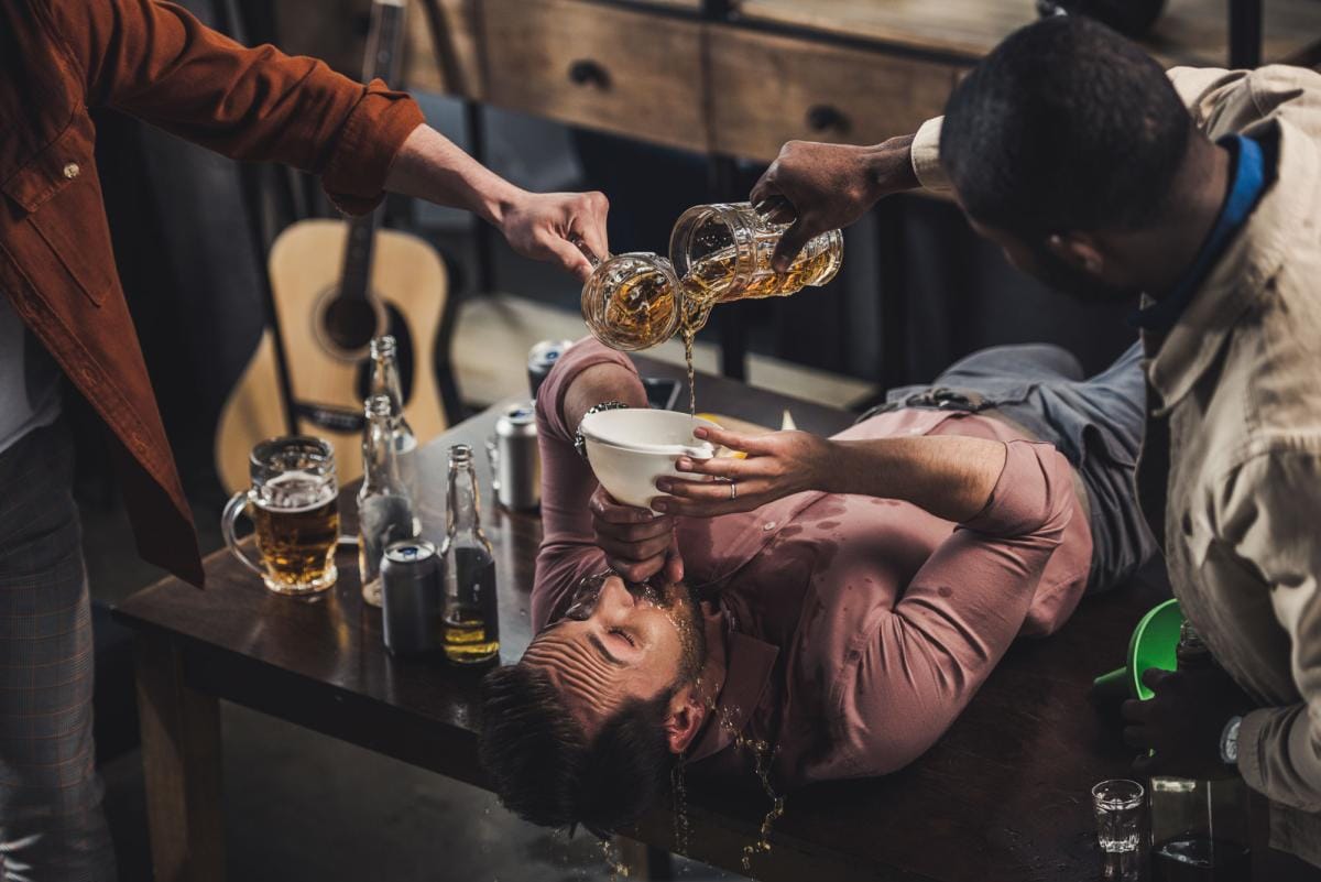 Man lying on bar while friends pour beer into bowl