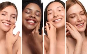 Four women of diverse ethnicities smiling and touching faces