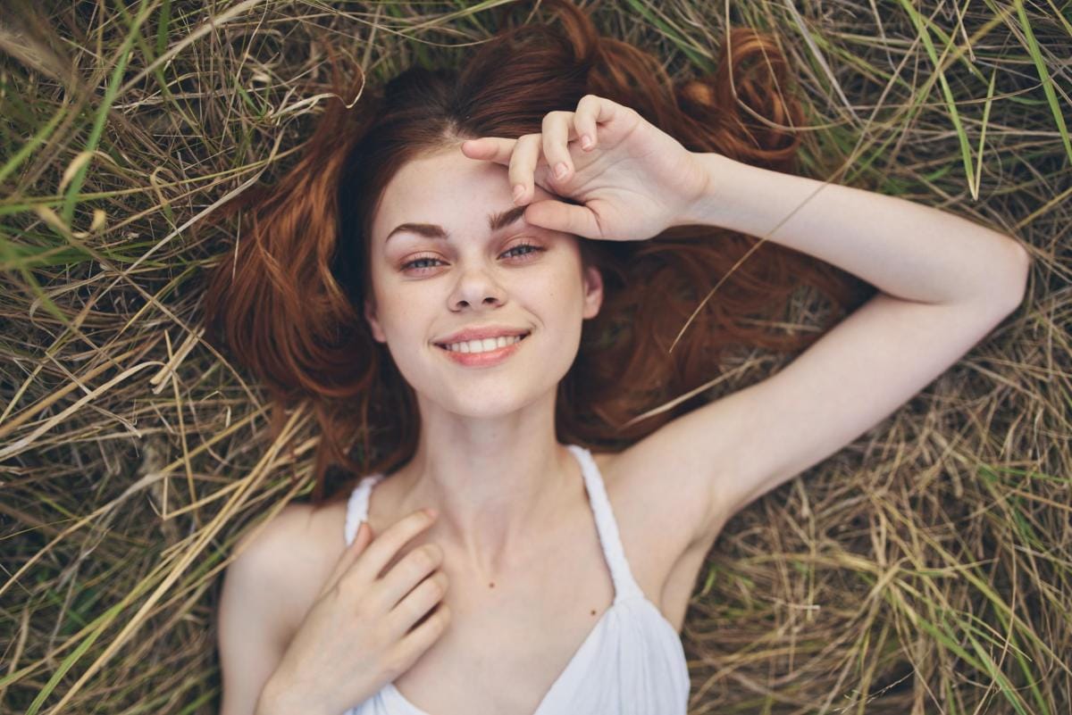 Smiling woman lying in grass with flowing red hair