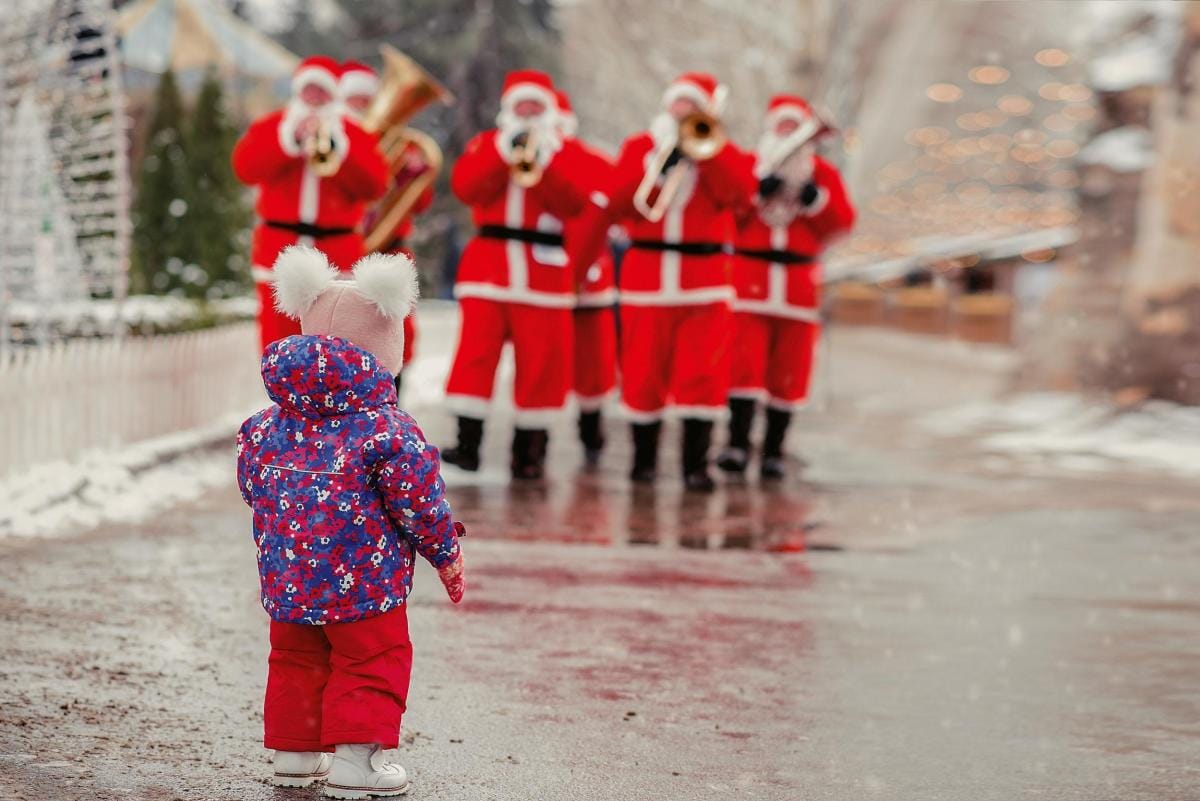 Toddler watching band of Santas playing trombones in snow