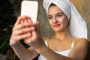 Woman with towel taking selfie with skincare cream