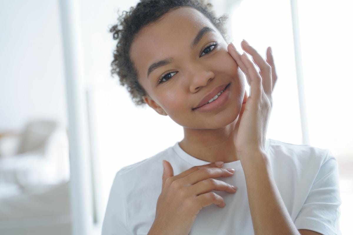 Young woman smiling gently, touching her face