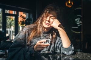 Woman resting chin on hand holding glass of water