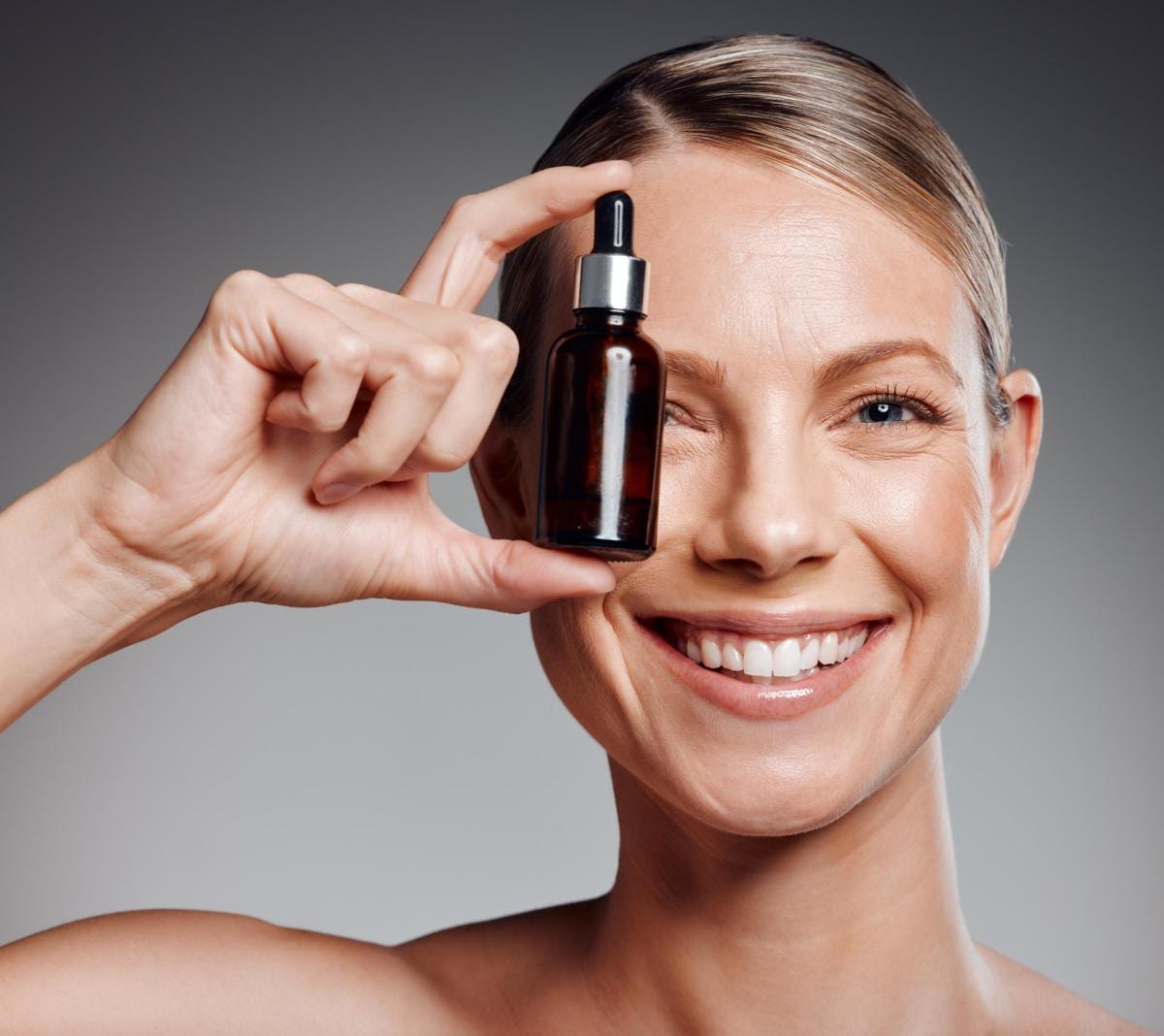 Smiling woman holding skincare serum bottle near eye