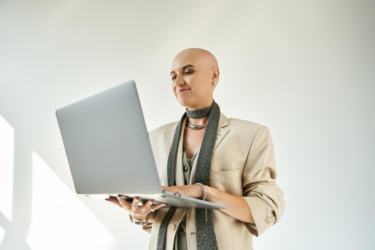 Bald woman smiling, using laptop in bright office