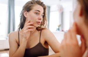 Woman examining acne in mirror