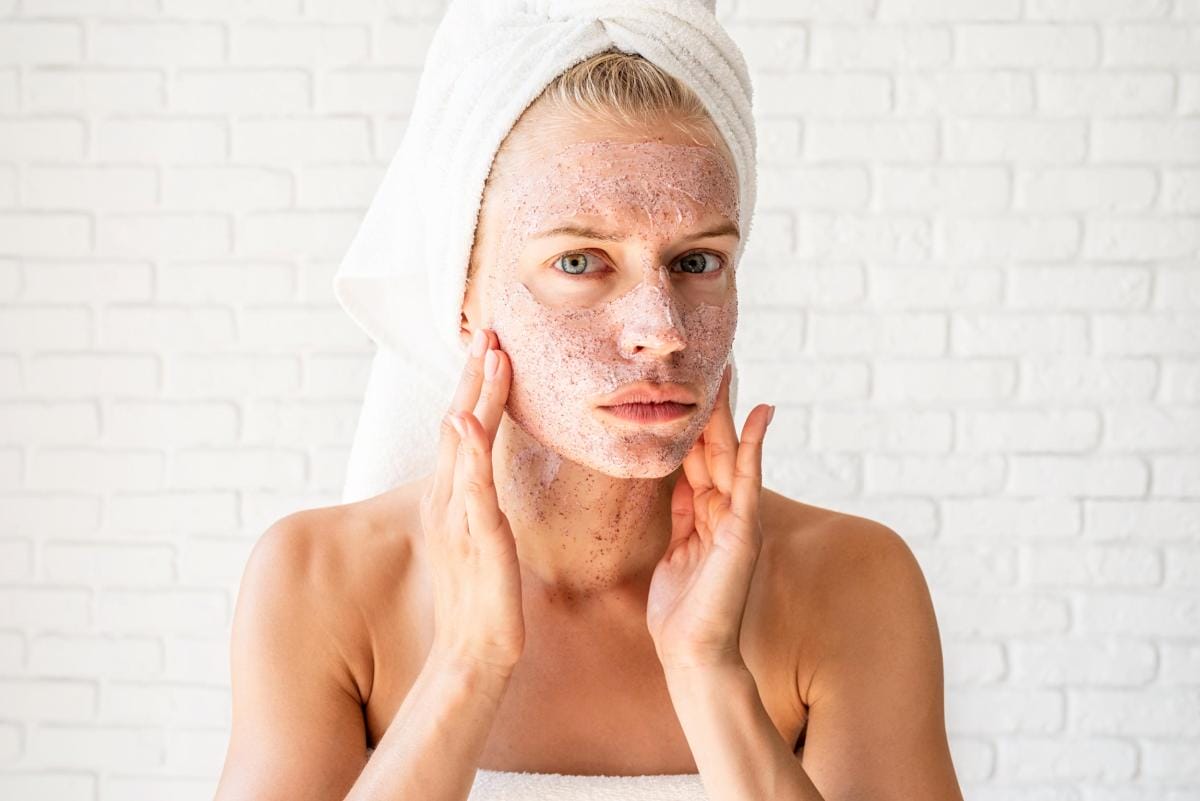 Woman applying facial scrub towel on head brick background