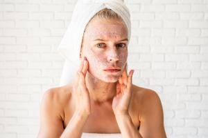 Woman applying facial scrub towel on head brick background