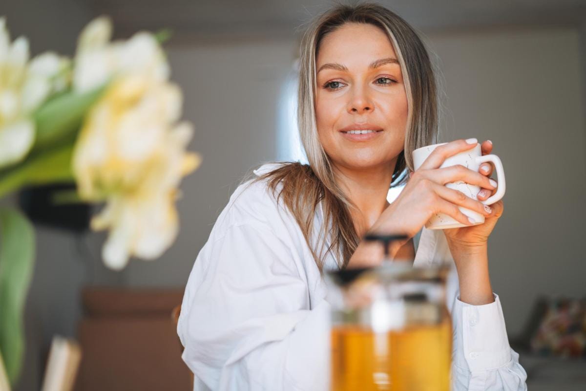 Woman smiling, holding coffee mug at home