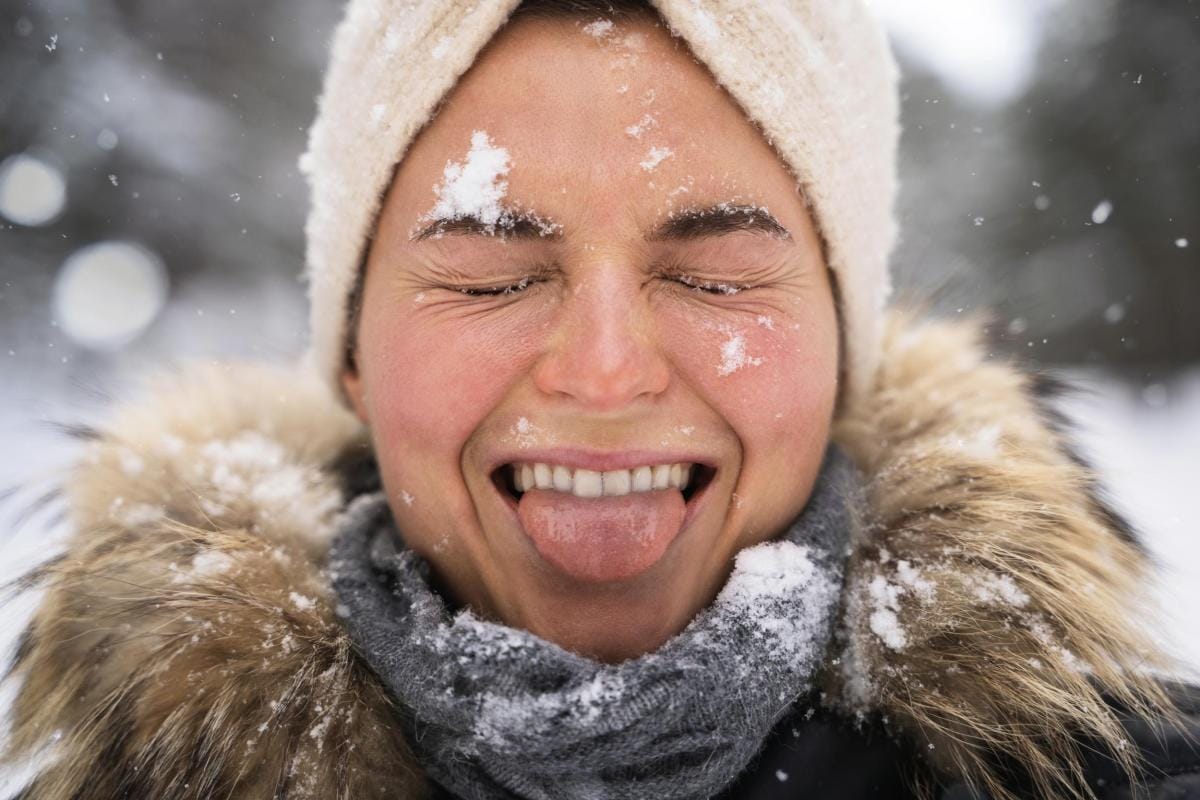 Joyful woman catching snowflakes with tongue in winter