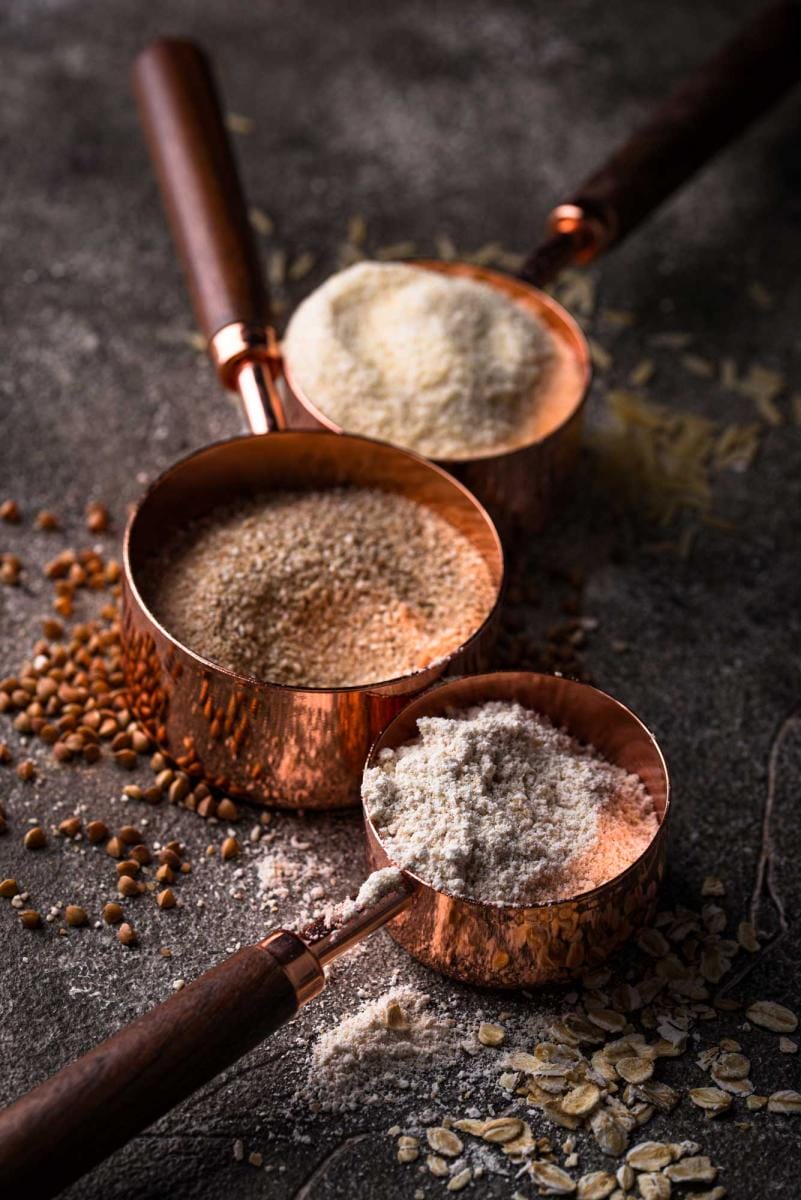 Copper scoops with flour and grains on dark surface