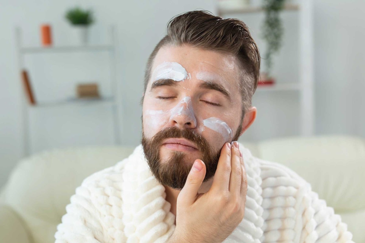 Man applying facial cream in a cozy room.