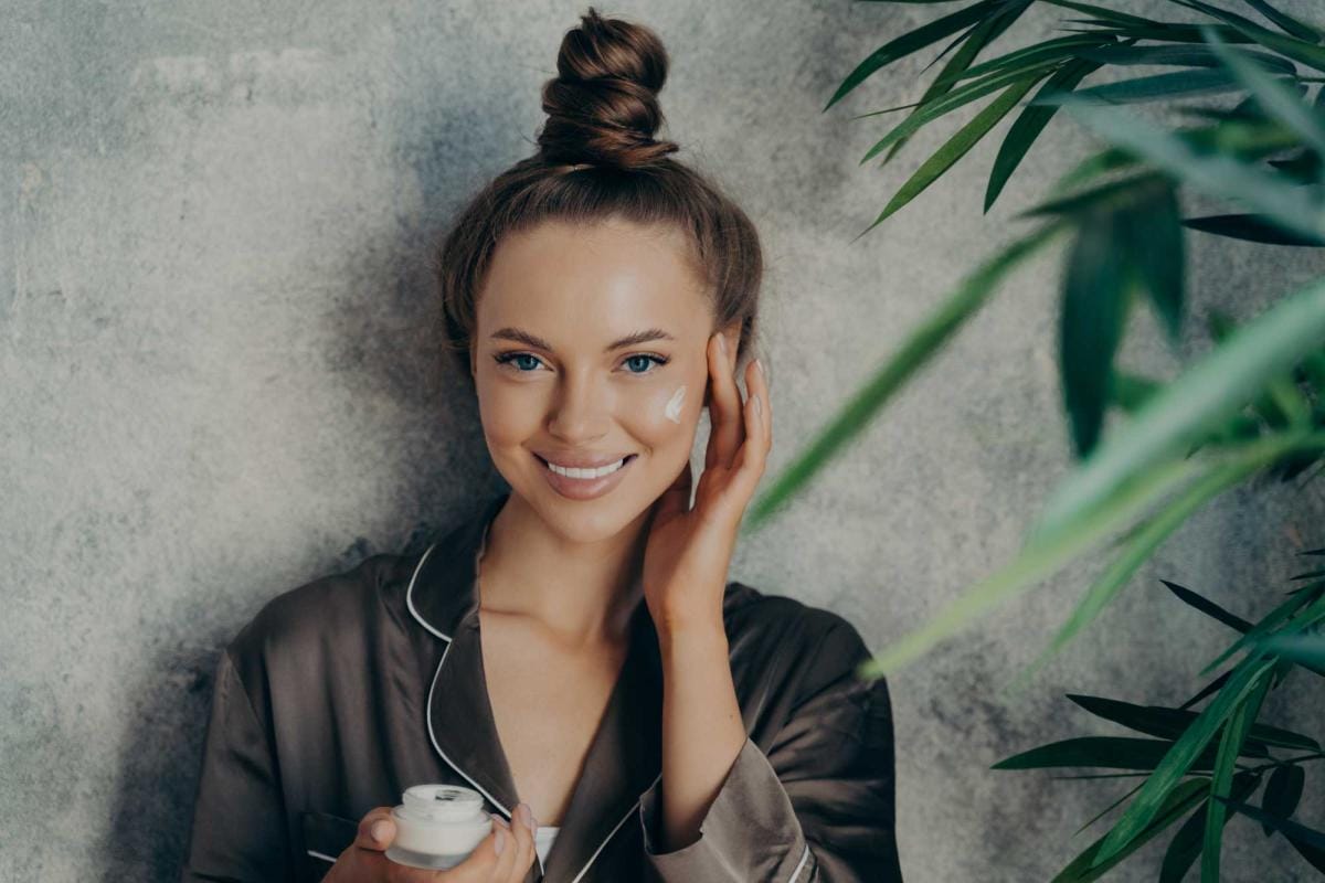 Woman applying cream, smiling with green plants