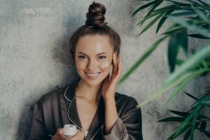 Woman applying cream, smiling with green plants