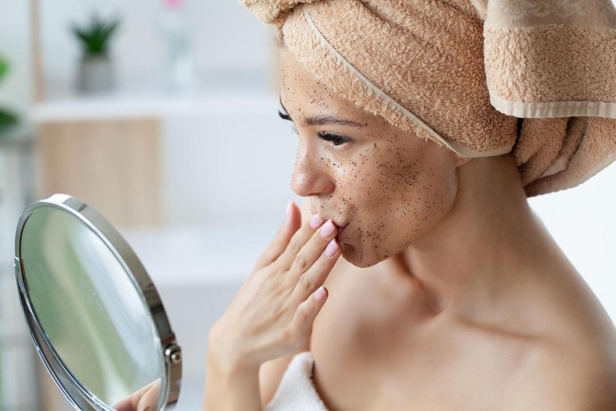 Woman examining face with scrub in mirror