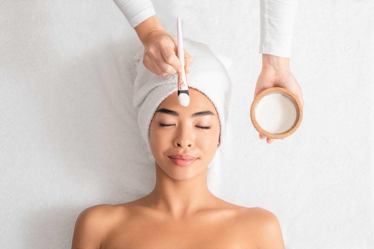 Woman receiving facial treatment with brush and cream