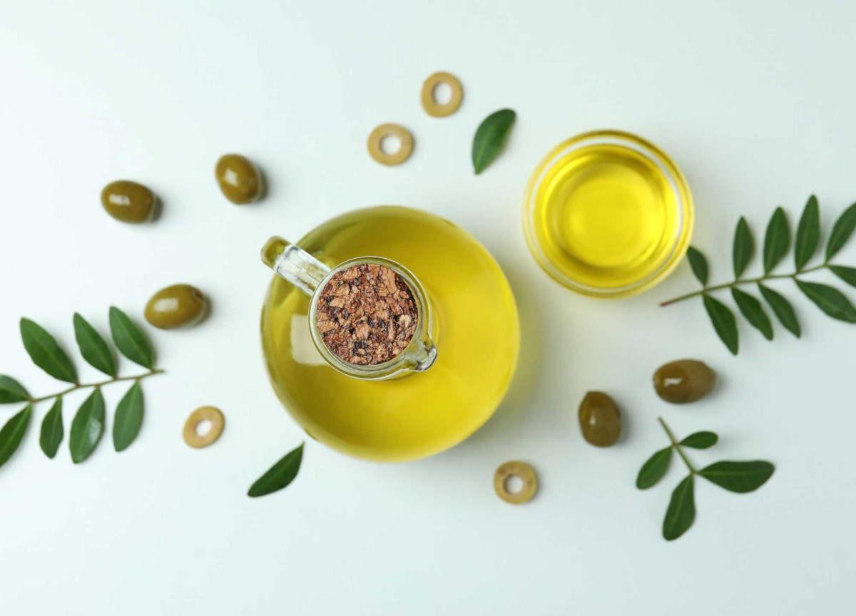 Olive oil in glass jug with fresh olives around