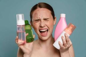 Frustrated woman holding various skincare products, acne visible