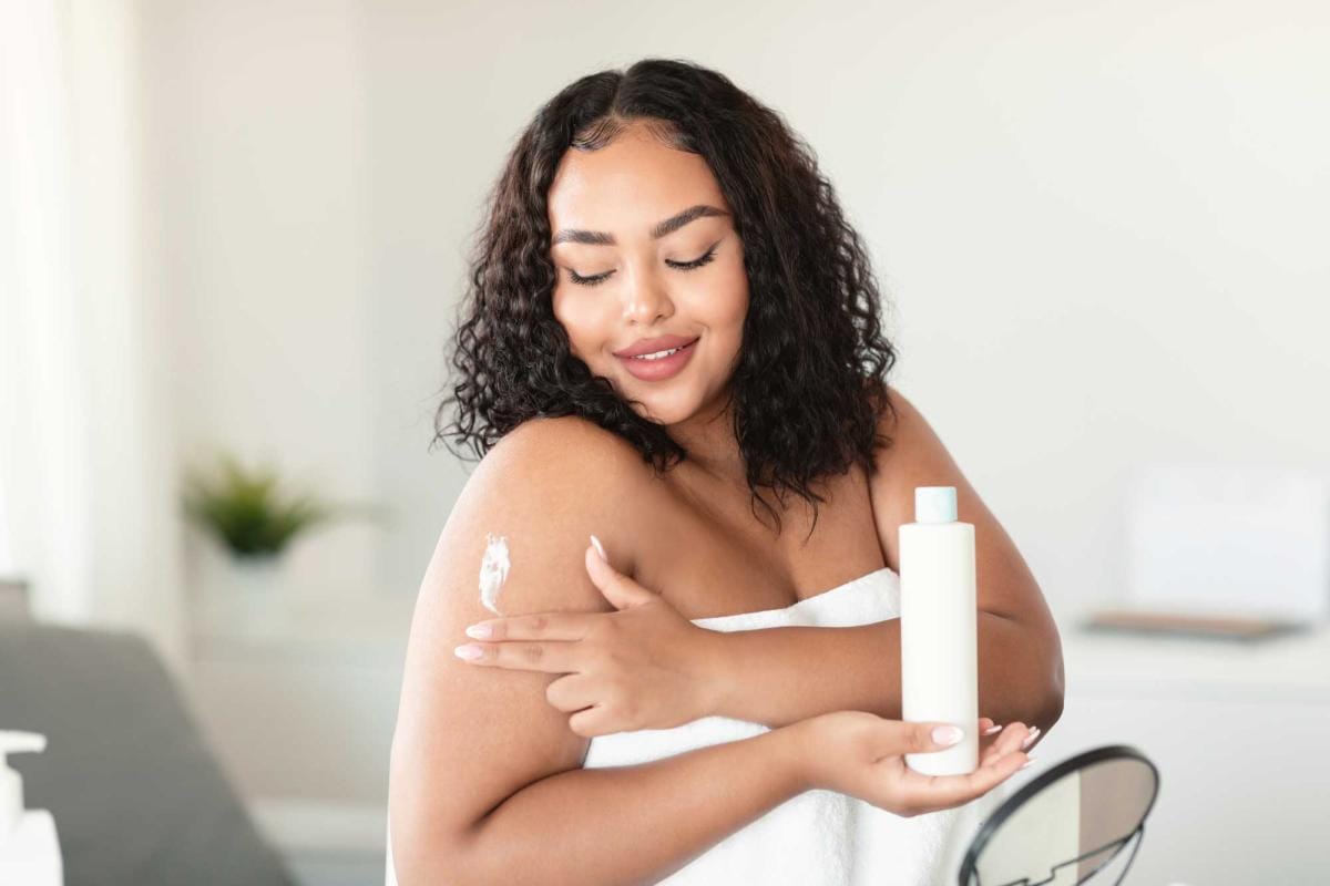 Woman applying lotion smiling in a bathroom