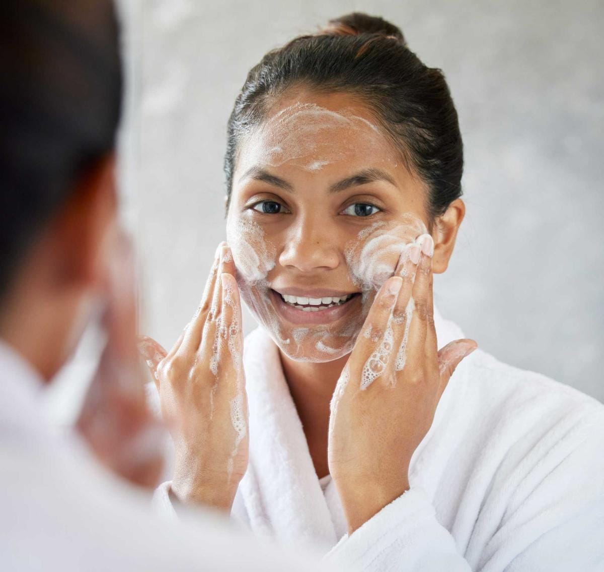 Woman applying facial cleanser in front of mirror